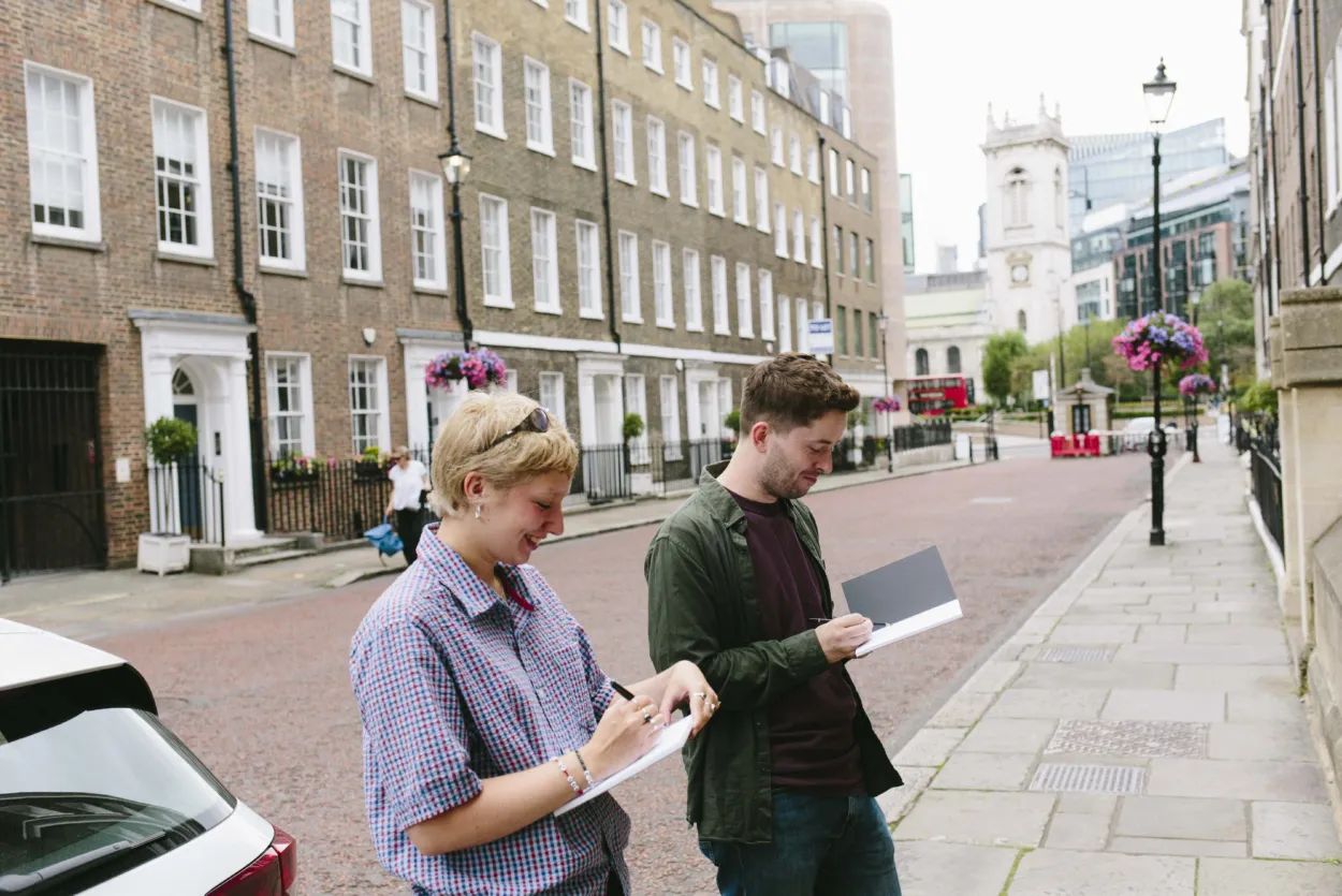 Adults on a sketch crawl with sketchbooks in hand focusing and drawing something on the opposite street out of view.