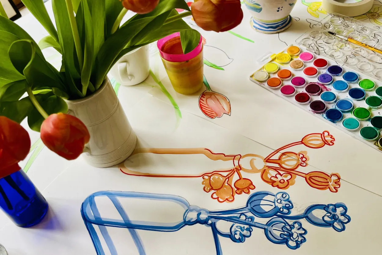 a table with paper and someone drawing a vase of flowers
