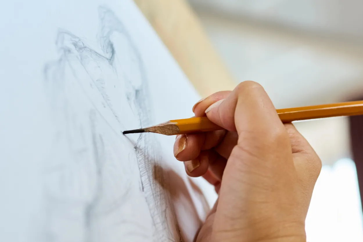 Close up of hand sketching life drawing model on white paper with a yellow pencil
