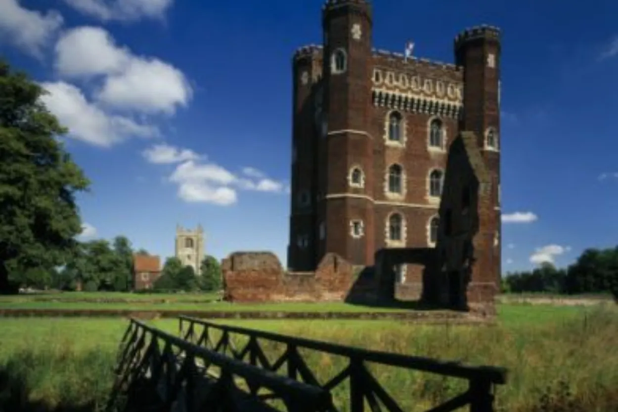 Tattershall Castle reflected in the moat on a bright day, with its striking red-brick tower rising above the surrounding landscape and greenery.
