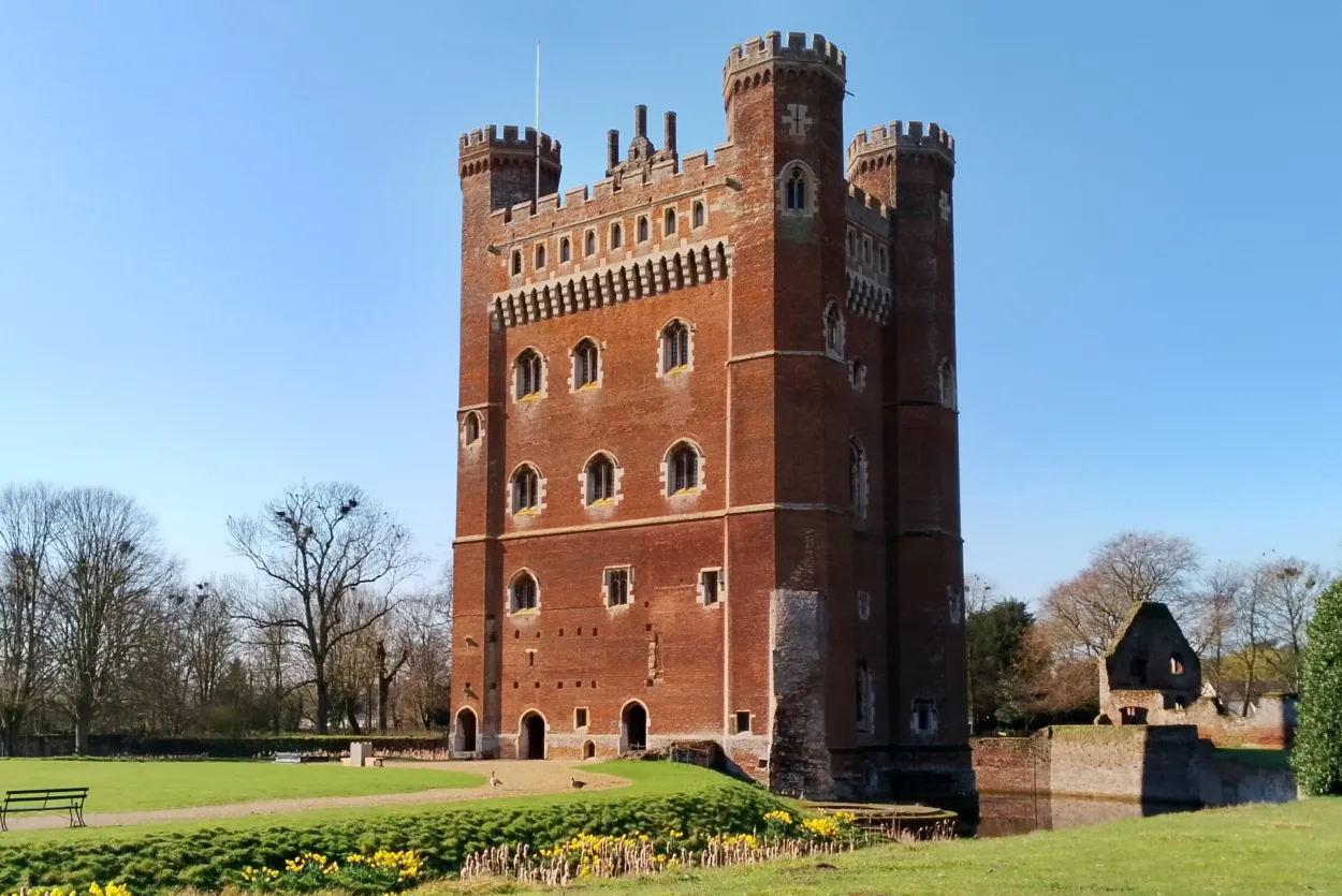 Tattershall Castle reflected in the moat on a bright day, with its striking red-brick tower rising above the surrounding landscape and greenery.