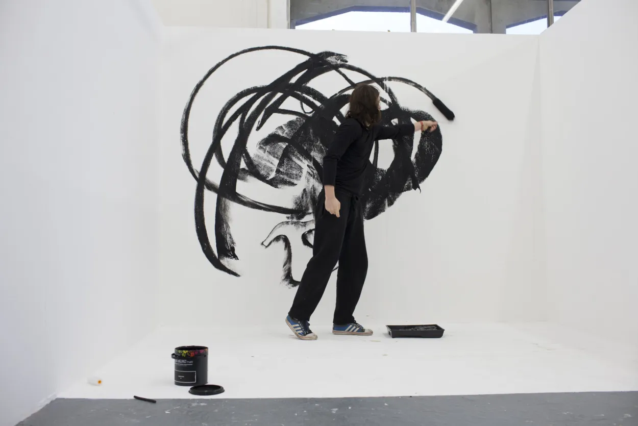 A man is drawing gestural, circular, marks in ink on a very large white canvas