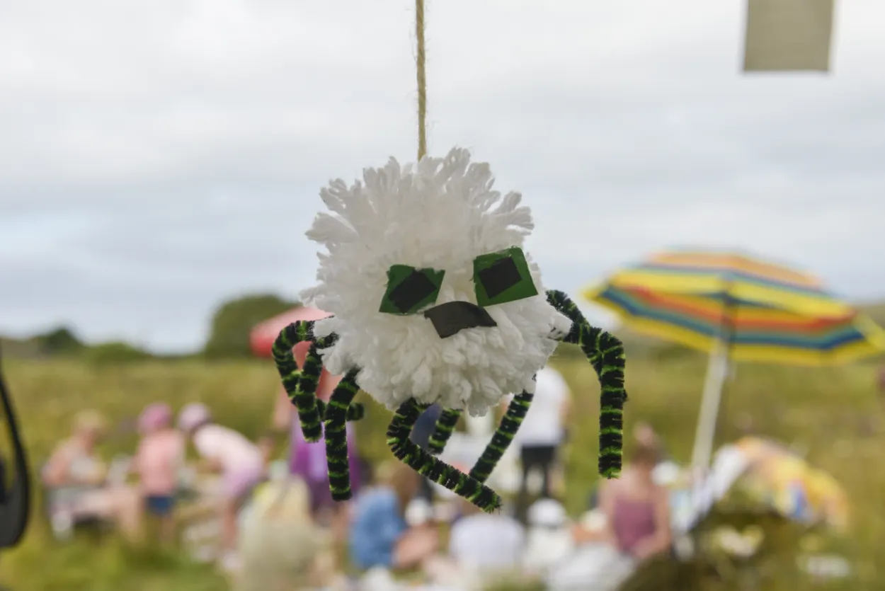 Hanging homemade white pom pom spider with pip cleaner legs. Umbrella in the background which is in a meadow.
