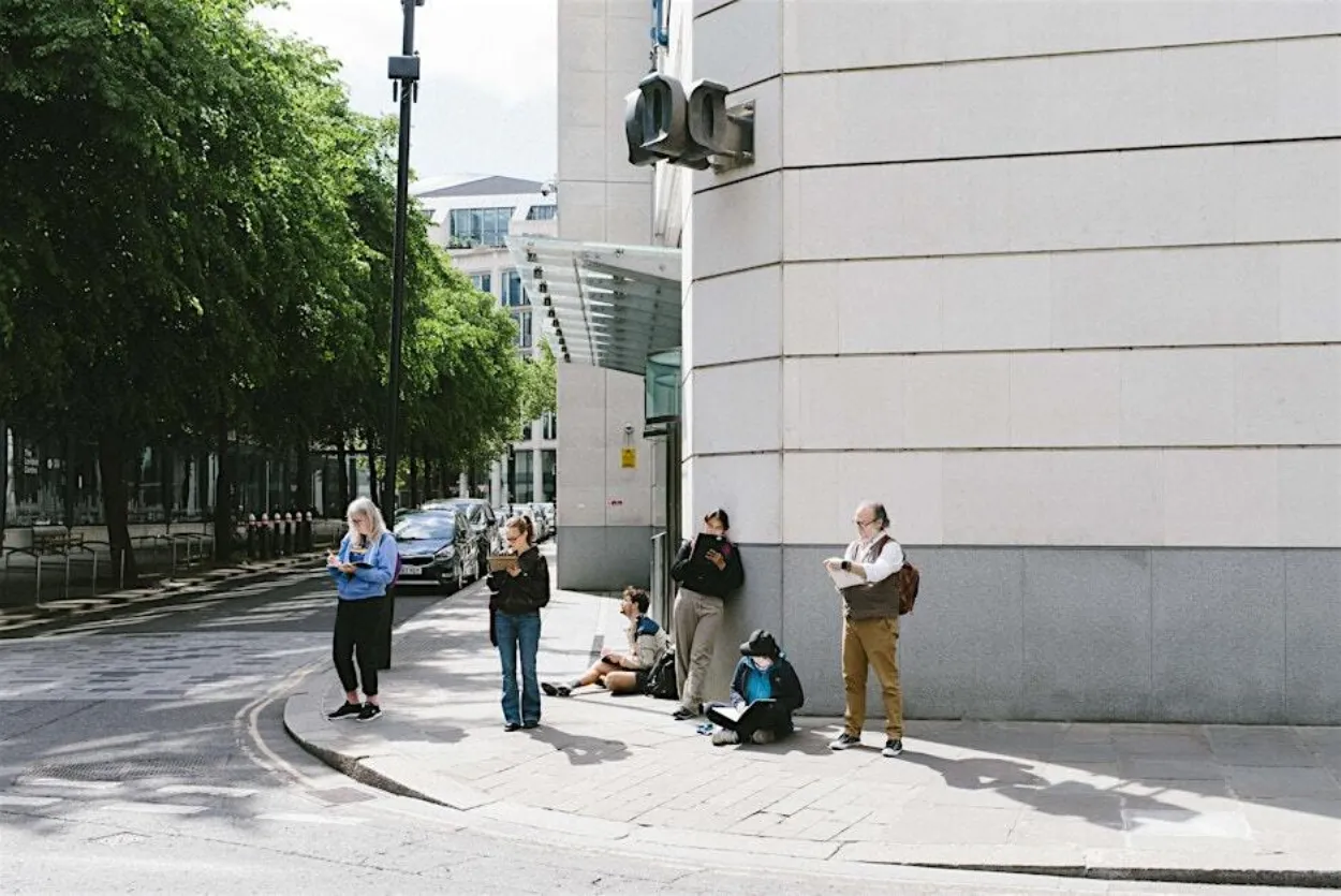 Adults on a sketch crawl with sketchbooks in hand focusing and drawing something on the opposite street out of view.