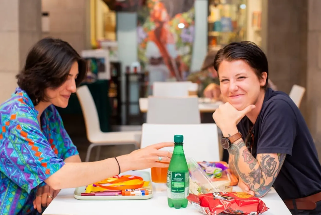 Two smiling individuals sitting at a table filled with snacks and art supplies