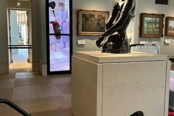 A museum stool with a sketchbook on top sits in front of a sculpture of the top half of a woman holding a fan - Meum with a Fan by Jacob Epstein