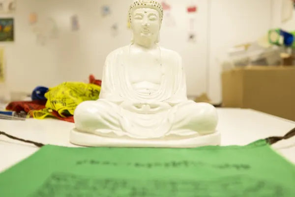 A small white Budda sits behind a green prayer mat