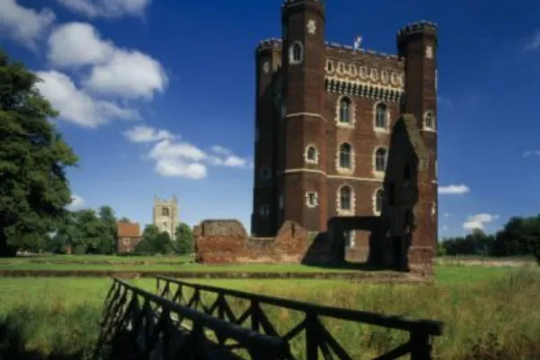 Tattershall Castle reflected in the moat on a bright day, with its striking red-brick tower rising above the surrounding landscape and greenery.