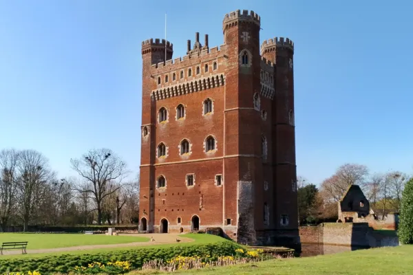 Tattershall Castle reflected in the moat on a bright day, with its striking red-brick tower rising above the surrounding landscape and greenery.