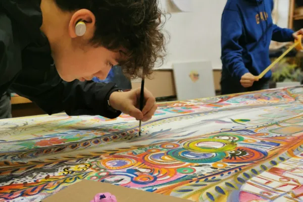 Young boy shown painting on a large collaborative piece.
