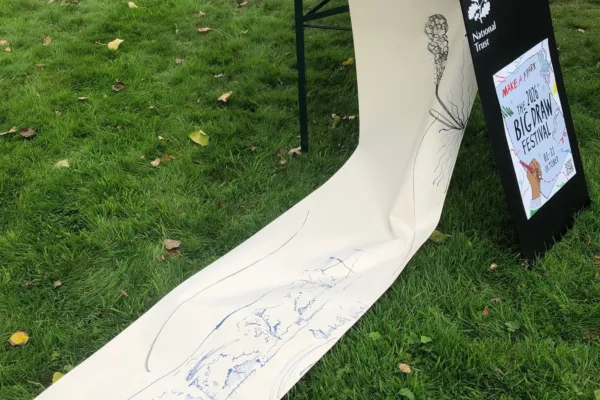 A large roll of paper with ink marks and drawing, hanging off a table with a poster for The Big Draw 2026 beside it.