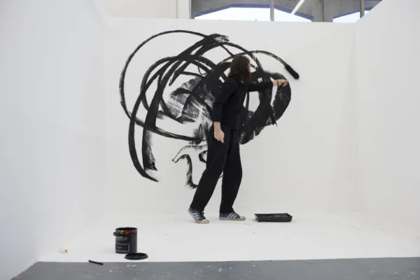 A man is drawing gestural, circular, marks in ink on a very large white canvas