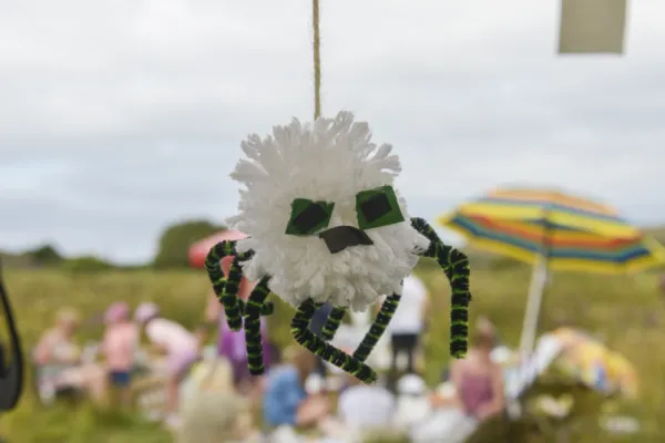 Hanging homemade white pom pom spider with pip cleaner legs. Umbrella in the background which is in a meadow.
