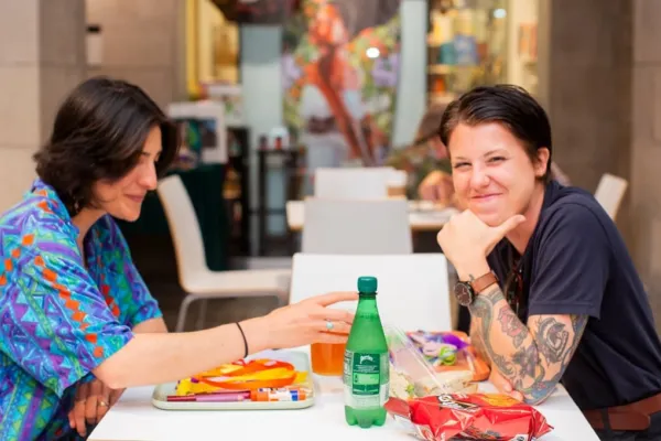 Two smiling individuals sitting at a table filled with snacks and art supplies