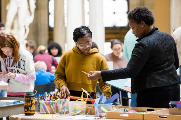 Several people standing at a crafts table picking up art-making supplies in the Sculpture Court of the Walters Art Museum.