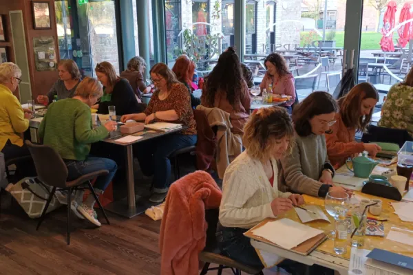 A group of participants sketching in groups of six around tables in a restaurant/bar